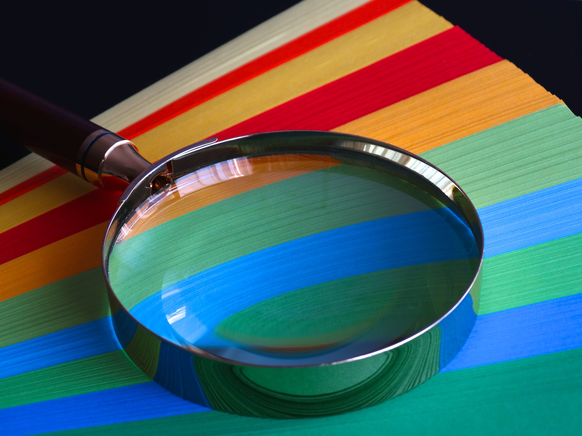Ett förstoringsglas ligger ovanpå papper i olika färger formade som en solfjäder.